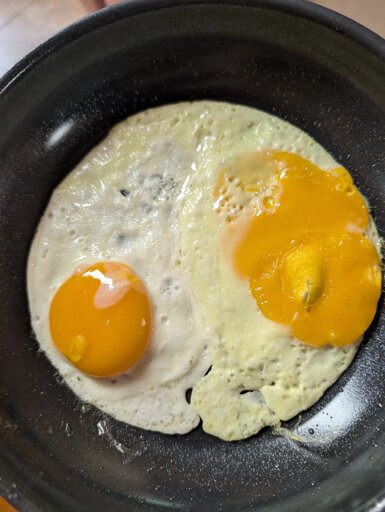 Photo is of two fried eggs in a nonstick pan, the right egg the yolk has broken and the white is distinctly yellow in hue, while the left egg is normal.